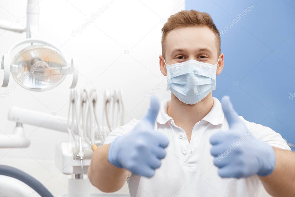 Always professional! Professional dentist wearing protective mask and gloves showing thumbs up posing at his dental clinic copyspace professionalism gesture approved confidence medicine health people 