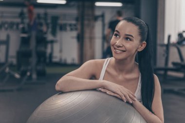 Uzak sevinçle seyir gülümseyen spor salonunda fitness topu üzerinde egzersiz sonra dinlenme sevimli mutlu genç kadın. Neşeli güzel sporcumuz egzersiz yaptıktan sonra kopya alanı rahatlatıcı. Sağlık kavramı