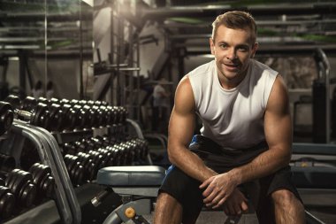 Spor salonu oturumdan sonra. Oturan adam neşeli yakışıklı genç fitness salonunda sevinçle gülümseyen boşaltmak motivasyon güven spor yaşam tarzı mutluluk aktif insanlar kavramı onun egzersiz yaptıktan sonra rahat.
