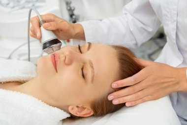 Dermatoloji taze pürüzsüz rekreasyon spa salonu profesyonellik pampering profesyonel güzellik uzmanı refah tarafından ultrasonik yüz cilt bakım tedavi alırken gülümseyen güzel genç kadın