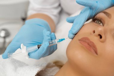 Güzel bir genç kadının Güzellik yüz tedavi kliniği plastik cerrahi botox şırınga enjektör steril meslek yordamda onun yüzüne dolgu enjeksiyonu getting yakın kırpılmış 