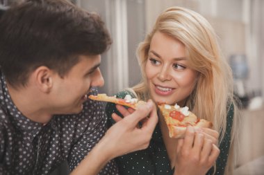 Birlikte lezzetli pizza yerken erkek arkadaşına, sevinçle gülümseyen güzel sarışın bir kadın. Güzel çift romantik bir akşam yeme keyfini. Sevgililer günü, çiftler, gıda kavramı