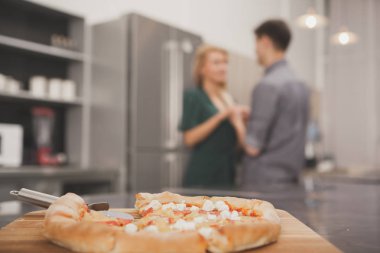 Seçici odak üstünde lezzetli taze pizza, arka plan üzerinde el ele tutuşarak mutlu sevgi dolu çift yaptı. Çift Romantik akşam yemeği evde emrini pizza ile hazırlanıyor. Yemek Servisi, eğlence kavramı