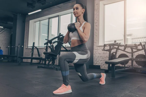 Low angle shot of a sporty young woman doing lunges with kettlebell. Attractive sportswoman enjoying working out at the gym, copy space. Fitness female in sportswear training with weights