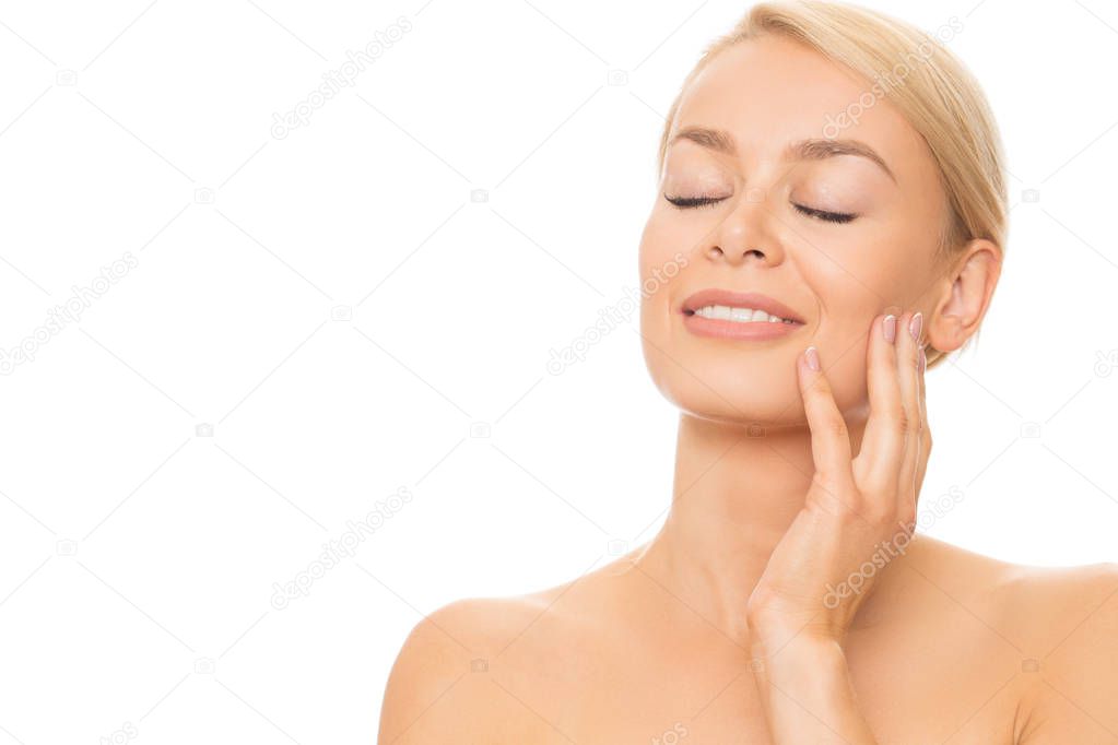 Young gorgeous blond haired woman smiling joyfully with her eyes closed touching herface gently isolated copyspace beauty soft smooth healthy flawless unblemished perfect skin skincare natural cosmetic