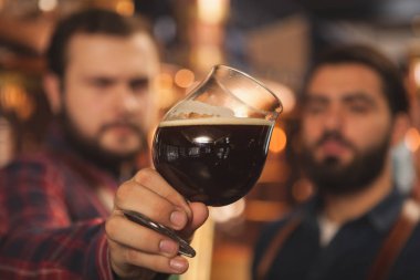 İki bira bir cam lezzetli dark bira inceleyerek bira üretim fabrikasında çalışan görüntüsünü kapatın. Seçici odak beermakers elinde bir bira bardağı. Kalite, uzmanlık kavramı