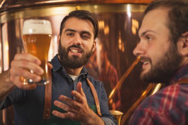Yakışıklı sakallı brewer gülümseyerek, zanaat bira demlenmiş taze inceleyerek süre meslektaşı için konuşuyor. İki beermakers MICROBREWERY çalışıyor. Yiyecek ve içecek üretim, küçük işletme kavramı