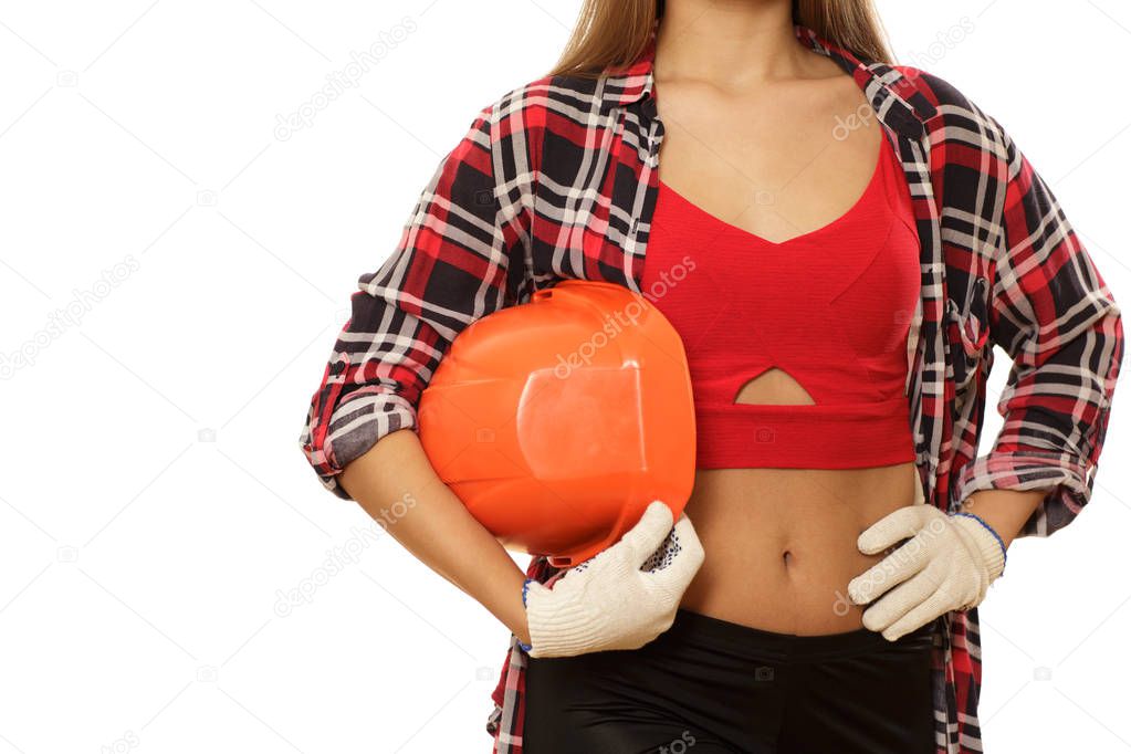 Cropped studio shot of a sexy female builder with perfect toned abs holding hardhat isolated. Young woman engineer with perfect body posing with a protective helmet. Safety, protection concept