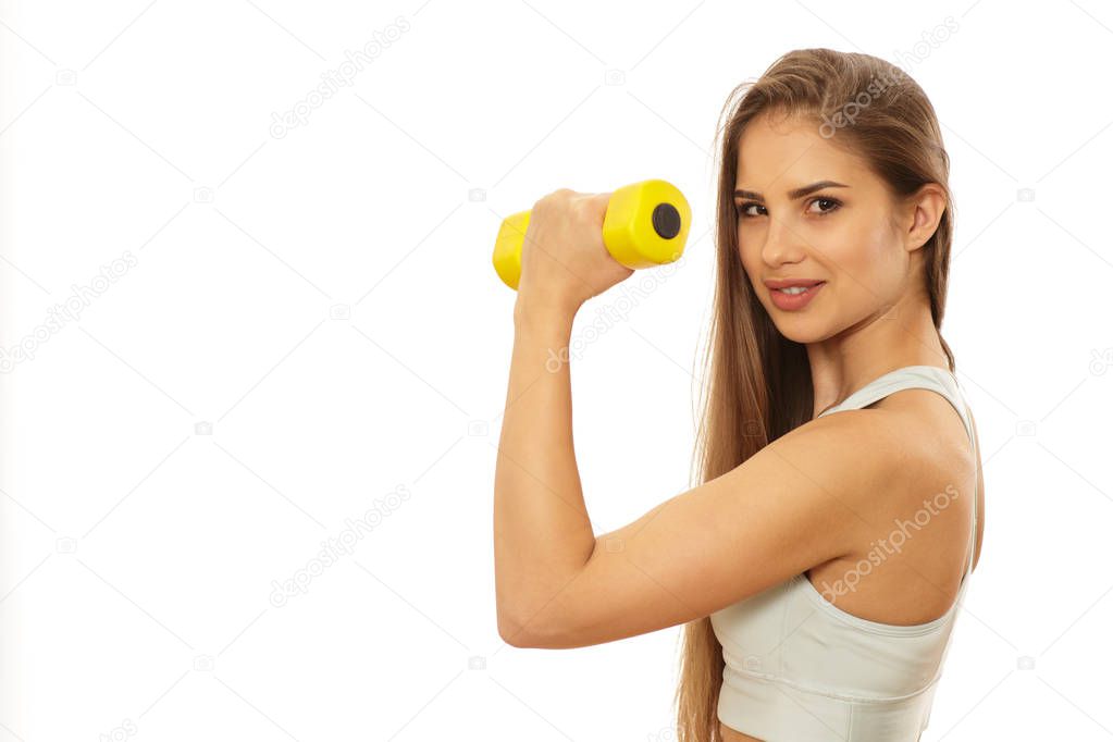 Beautiful athletic sexy woman smiling joyfully flexing her biceps holding a dumbbell isolated. Stunning fitness female working out with weights. Happy healthy sportswoman exercising
