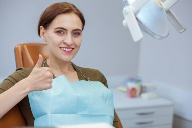 Kopya alanı gösteren başparmak, gülümseyen diş sandalyede oturan mutlu güzel kadın. Çekici bayan hasta başarılı oral tedavi sonra gülümseyerek. Mutluluk, sağlık, diş hekimliği kavramı