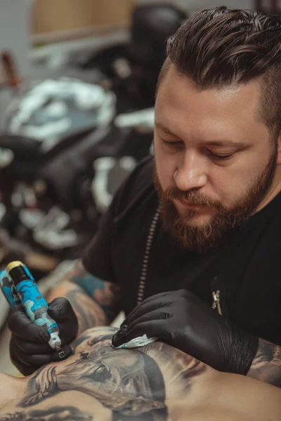 Бородатий татуювач робить татуювання на тілі свого клієнта — стокове фото
