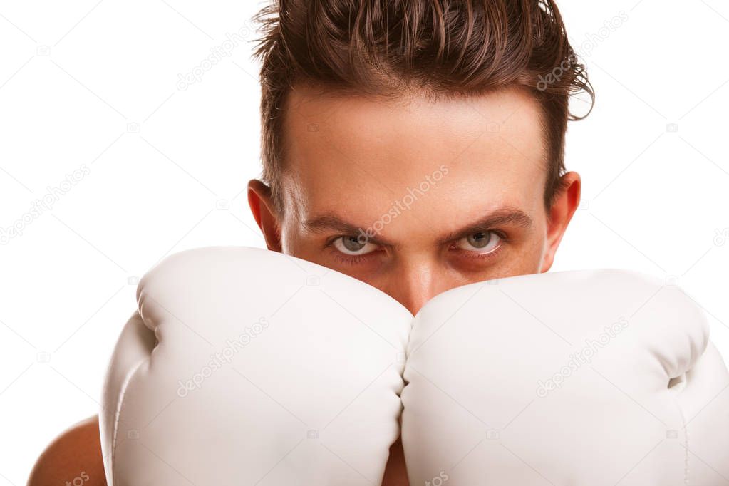 Close up of a male boxer covering his face with hands in boxing gloves, looking to the camera aggressively, ready to fight. Professional fighter looking confidently. Martial arts, defense concept