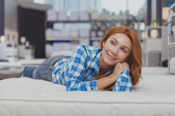 Hermosa mujer comprando nuevo colchón en la tienda de muebles — Foto de Stock