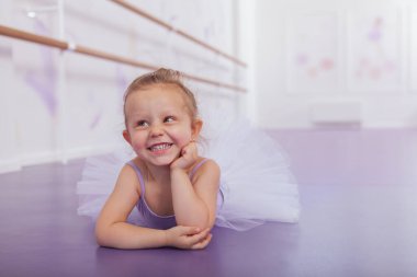 Küçük sevimli balerin kız gülüyor, başka tarafa bakıyor. Bale okulunda etek ve etek giymiş şirin mutlu küçük kız yerde uzanıyor, boşluğu kopyalıyor.