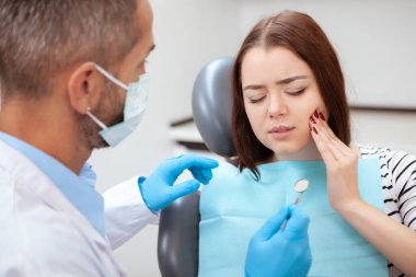 Dişi ağrıyan genç bir kadın, klinikte dişçi koltuğunda oturuyor. Diş ağrısı şikayetiyle gelen dişçi kadın hasta.