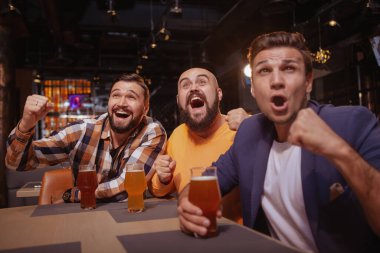 Bir grup arkadaş koşuşturuyor, bira barında futbol maçı izliyorlar. Erkek futbol taraftarları heyecanlı görünüyor, favori takımlarının zaferini kutluyorlar.