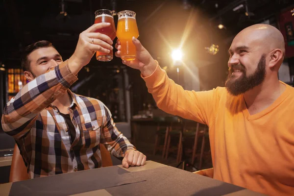 ビールのパブでお祝いする2人の男性の友人の低角度ショット 彼らの眼鏡をクリックして — ストック写真