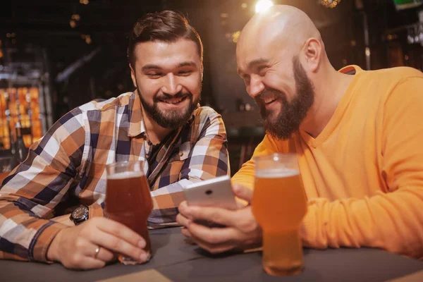 Twee Lachende Vrienden Met Een Smartphone Bierkroeg Opgewonden Man Toont — Stockfoto