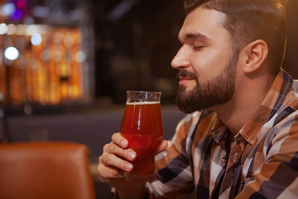 Close up profile shot of a handsome relaxed man smelling aroma of delicious beer in his glass. Happy man drinking at beer pub