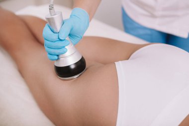 Bir kadın müşteriye rf-lift işlemi yapan bir güzellik uzmanının yakın çekimi. Bir kadın kalçasının arkasında rf-lift tedavisi görüyor.