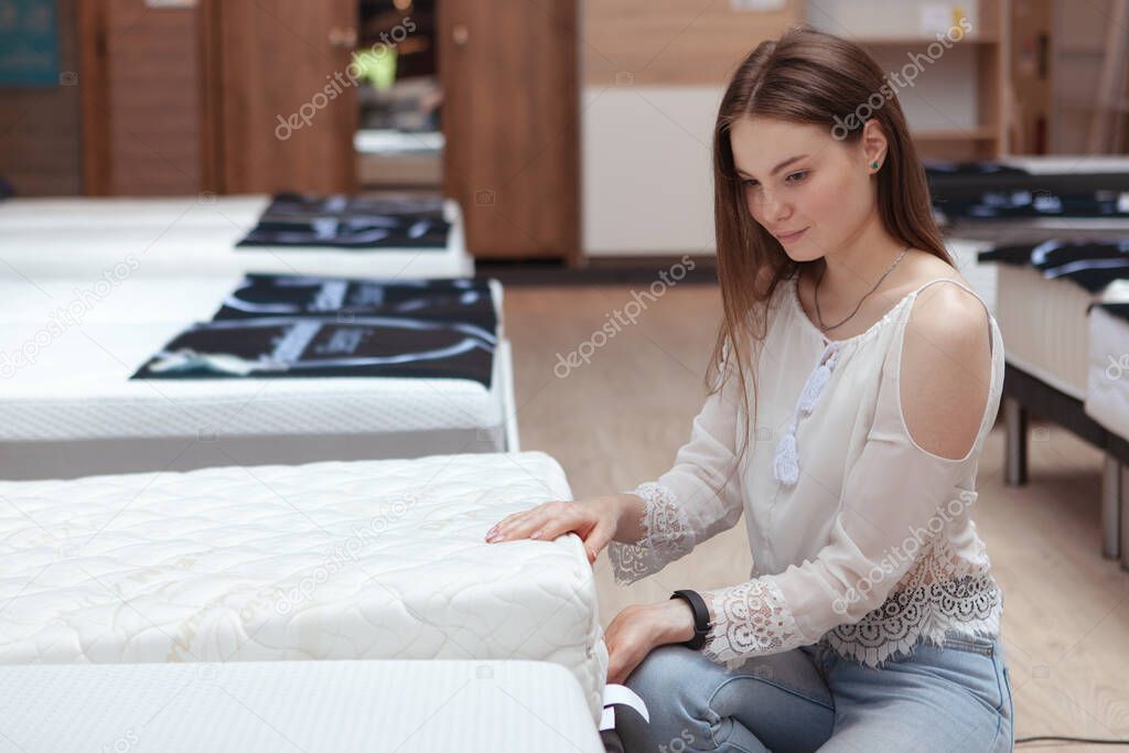 Beautiful young woman shopping for a new orthopedic bed at furniture store