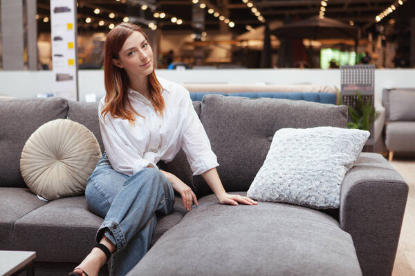 Очаровательная женщина сидит на новом диване в мебельном магазине
