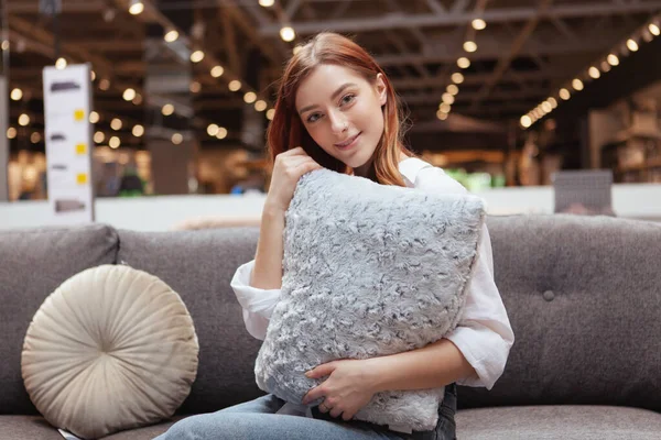 可爱而快乐的女人抱着枕头 坐在家具店的新沙发上 — 图库照片
