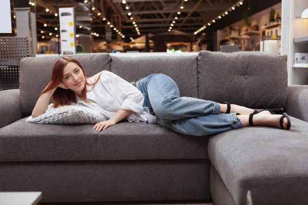 快乐美丽的女人笑着躺在家具店的沙发上 — 图库照片