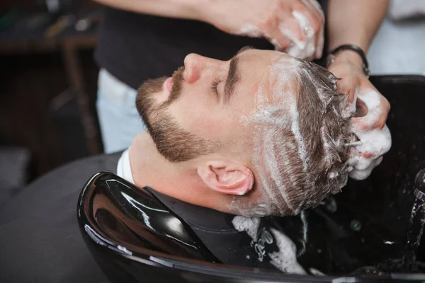 在理发师用洗发水洗头的时候 一个留着胡子的男人正在休息 — 图库照片