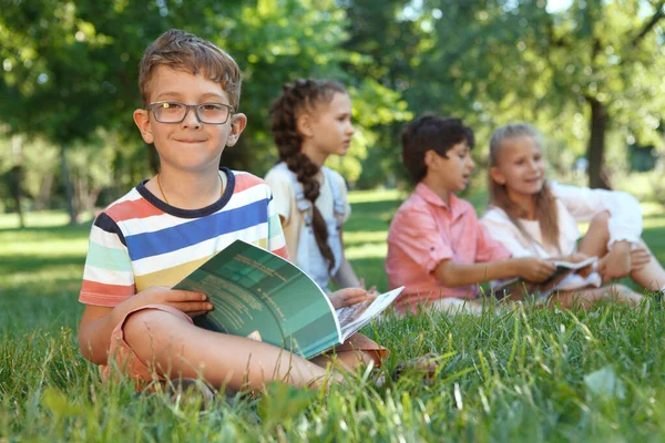 Charming Little Boy Smiling Camera While Reading Book Sitting Grass — Stock Photo, Image