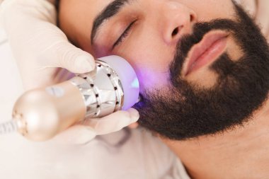 Sakallı bir adamın yaşlanma karşıtı donanım tedavisi görürken çekilmiş yüz bakımı.