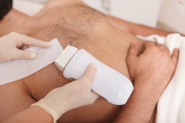 Sıcak balmumu ve kağıt şeritleri kullanarak erkek müşterinin göğüs kıllarını aldıran bir güzellik uzmanı.