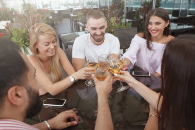 Bir grup arkadaş kadeh tokuşturuyor, çatıdaki restoranda içiyorlar.