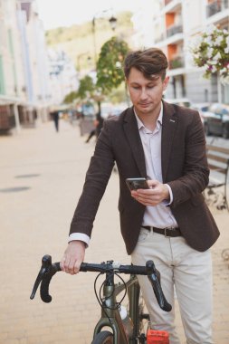 Yetişkin bir adamın akıllı telefonunu kullanırken, şehirde bisikletle dolaşırken dikey görüntüsü.