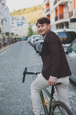 Neşeli bir adamın dikey dikiz görüntüsü. Etrafa bakıyor, şehirde bisiklet sürüyor.