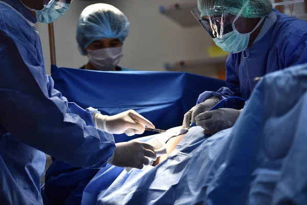 Team surgeon at work in operating room. Surgical light in the operating room. Preparation for the beginning of surgical operation with a cut. The surgeon is performing surgery on the patient.