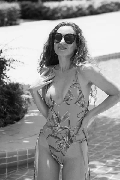 Güzel kız havuz başında güzel bir mayo parlak bir günde. Güzel zarif yanık tenli kadın bikini ve güneş gözlüğü yüzme havuzu Spa'da rahatlatıcı portresi. Sıcak yaz günü ve parlak güneşli ışık.