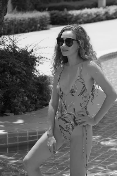 Güzel kız havuz başında güzel bir mayo parlak bir günde. Güzel zarif yanık tenli kadın bikini ve güneş gözlüğü yüzme havuzu Spa'da rahatlatıcı portresi. Sıcak yaz günü ve parlak güneşli ışık.