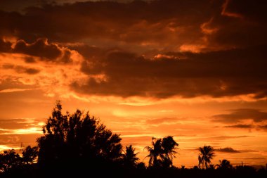 Dağın zirvesine günbatımı manzara. Turuncu-kırmızı bulutun turuncu gökyüzü ve üst üste gelen dağ manzaraları vardır.
