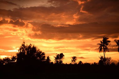 Dağın zirvesine günbatımı manzara. Turuncu-kırmızı bulutun turuncu gökyüzü ve üst üste gelen dağ manzaraları vardır.