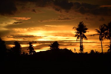 Dağın zirvesine günbatımı manzara. Turuncu-kırmızı bulutun turuncu gökyüzü ve üst üste gelen dağ manzaraları vardır.