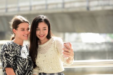 İki kız arkadaş cep telefonuyla selfie çekiyor.