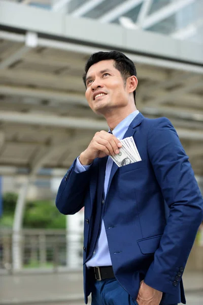 Asian businessman is throwing money to pocket of suit