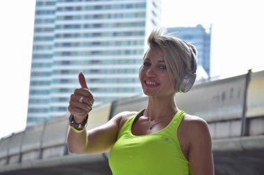 Kulaklıkla müzik dinleyen ve baş parmağını kaldıran bir spor kadını.