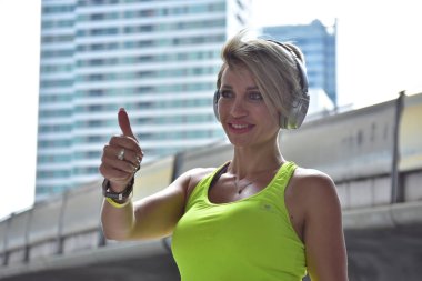 Kulaklıkla müzik dinleyen ve baş parmağını kaldıran bir spor kadını.