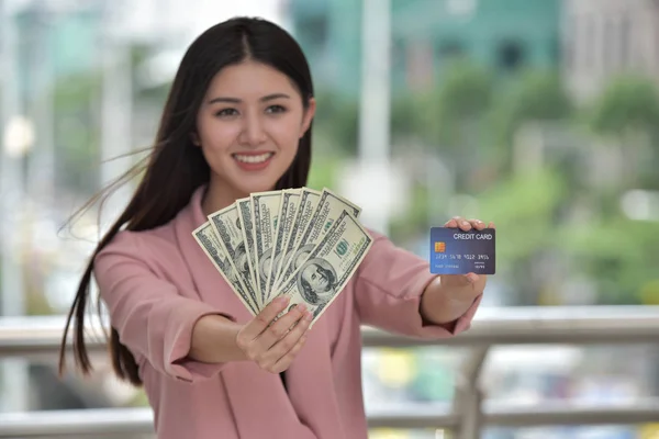 Asian woman is holding dollar banknotes and credit card