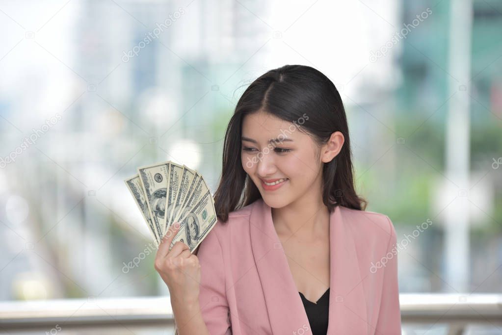 Asian girl in pink suit Send a sweet smile with hand holding many cash in hand 