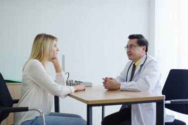 Doktor masadaki hasta kadınla konuşuyor.