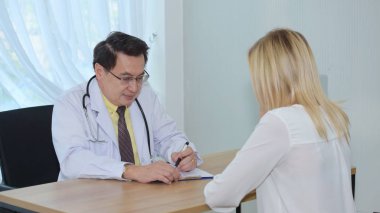 Doktor masadaki hasta kadınla konuşuyor.