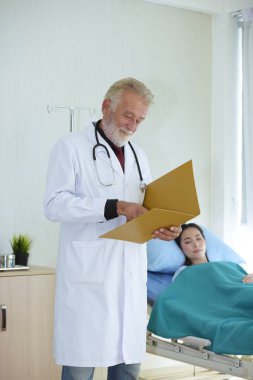 Elinde dosya olan doktor hastane odasını ziyaret ediyor.
